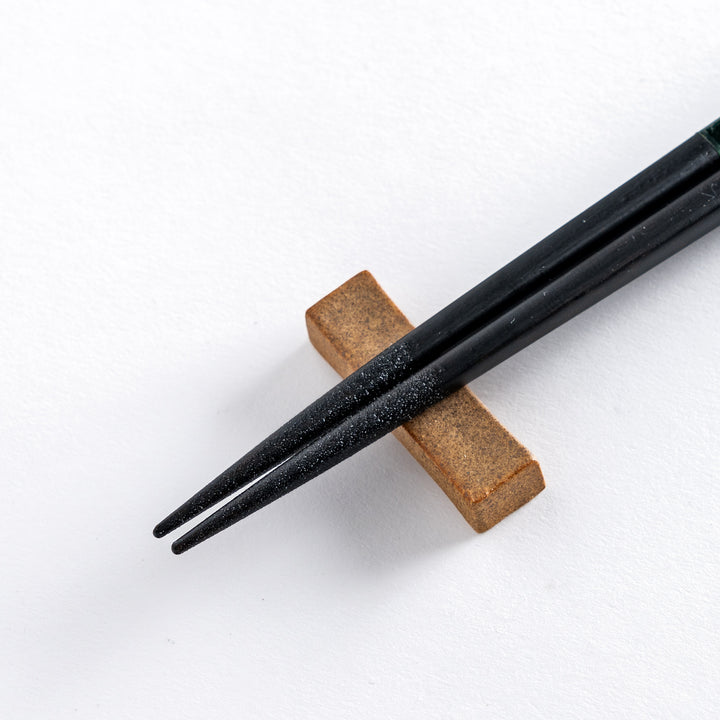 Close-up of Forest color chopstick tip resting on an earthy brown chopstick rest, showcasing intricate design and texture.