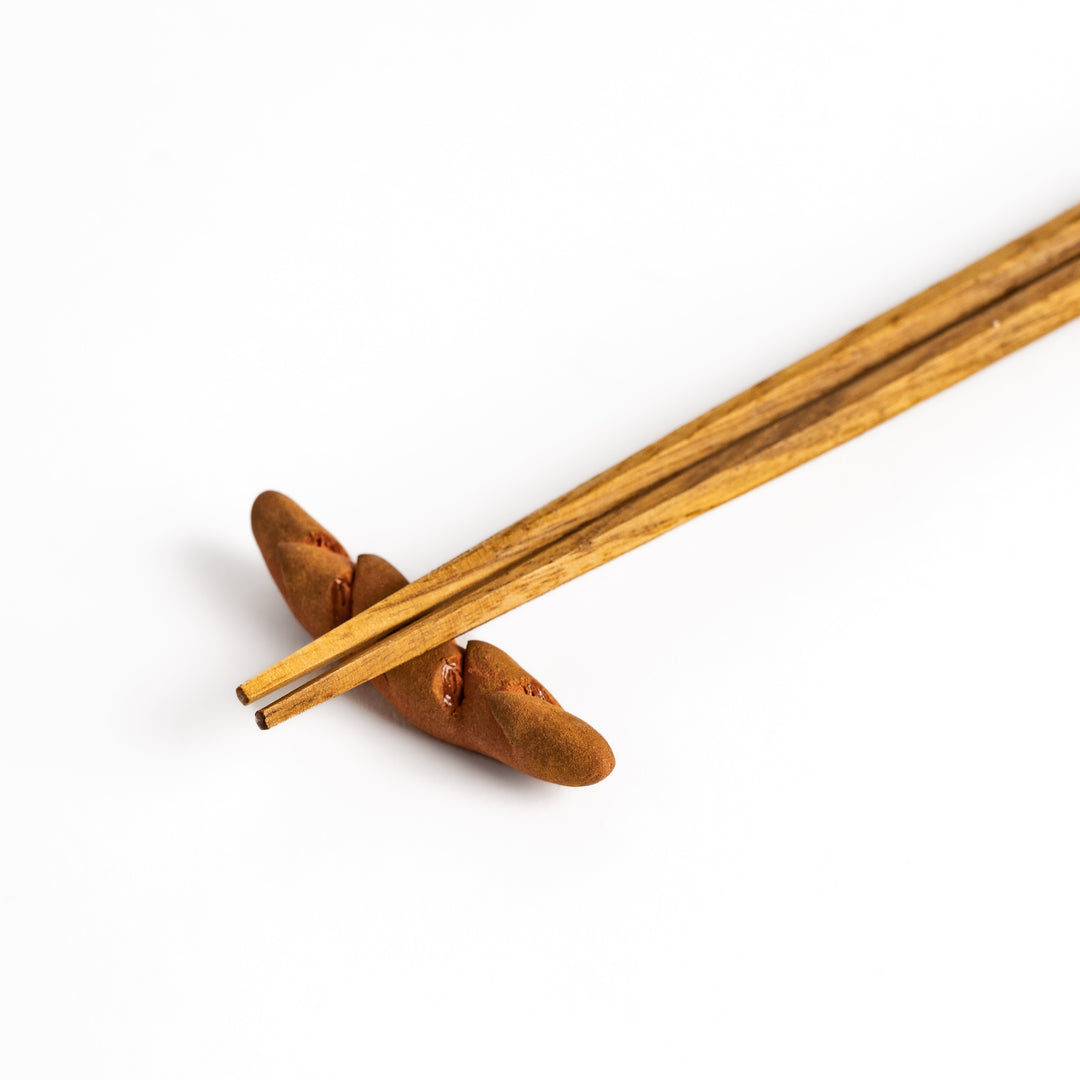 Epi Bread Chopstick Rest holding wooden chopsticks, showcasing its unique baguette design and practical functionality.