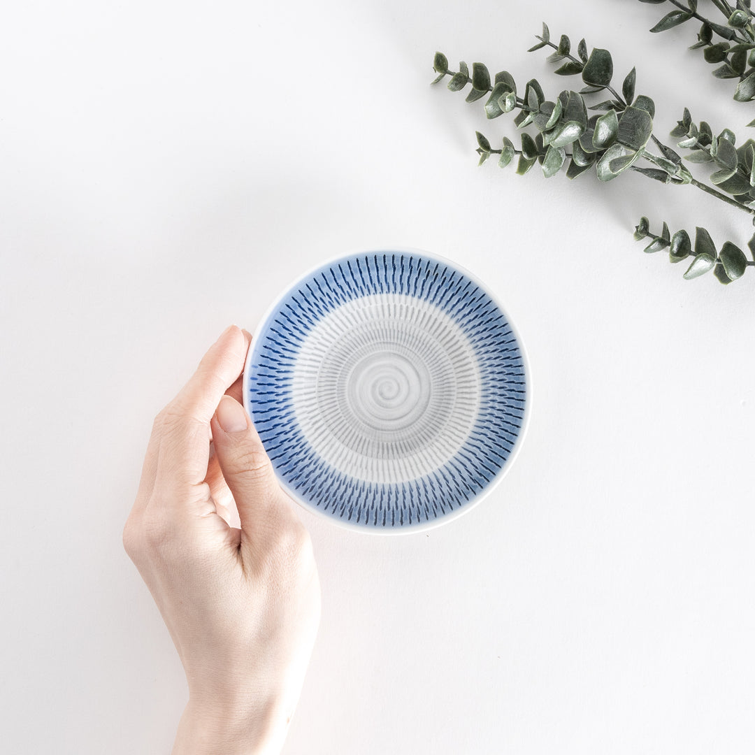 A hand holds the blue dessert plate, showcasing its striking spiral-striped design from above.