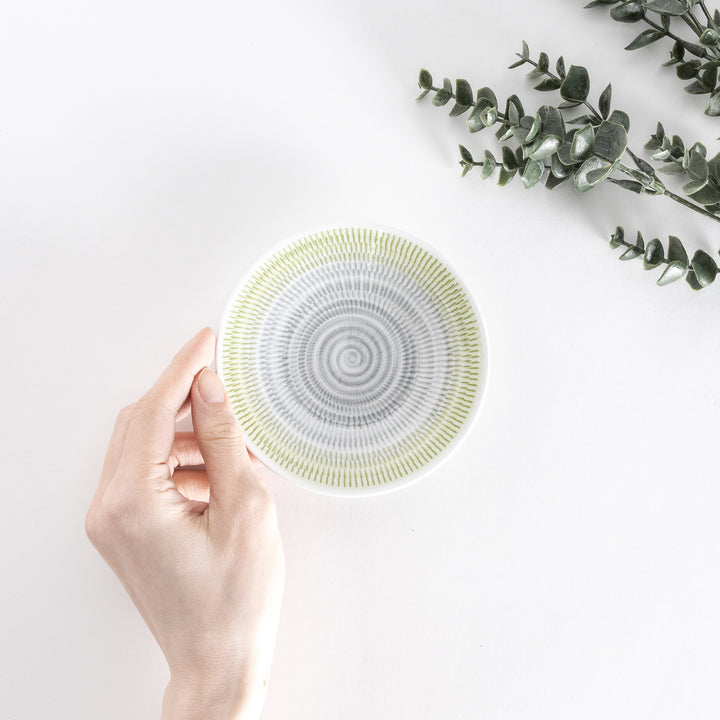 A hand holds the yellow-green dessert plate, displaying its gentle spiral-striped design from a top view.