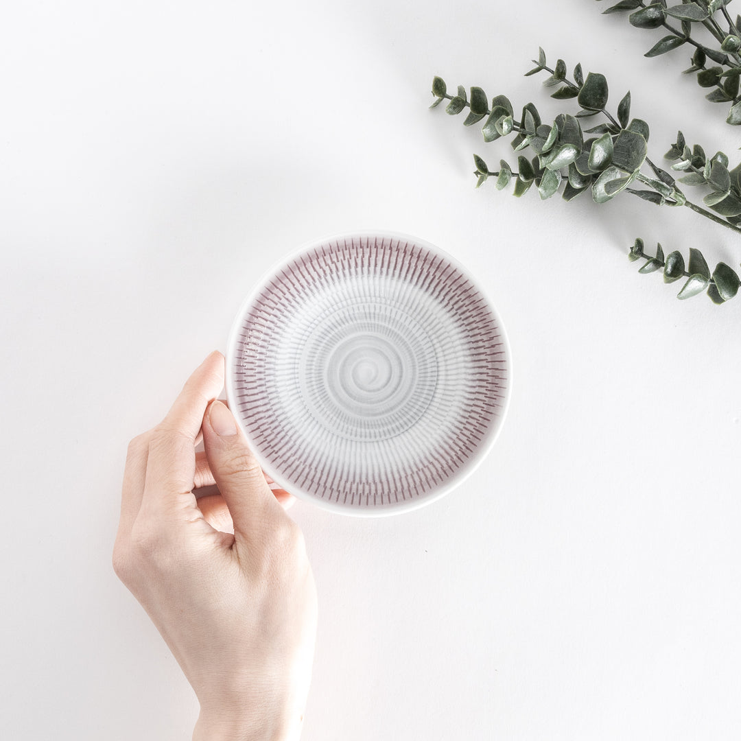 A hand holds the light purple dessert plate, showcasing its delicate spiral-striped design from above.