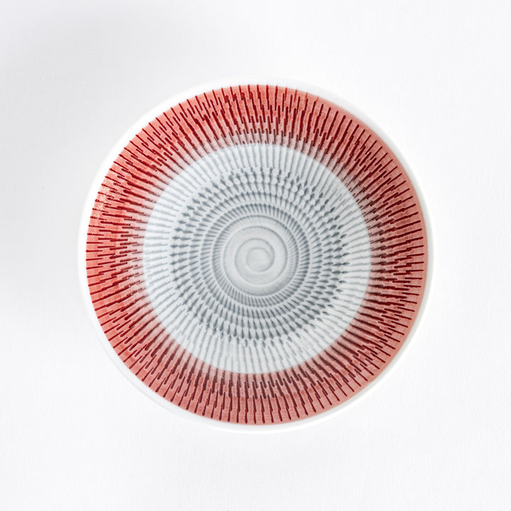 A red dessert plate with bold radiating spiral-striped patterns, captured from the front.