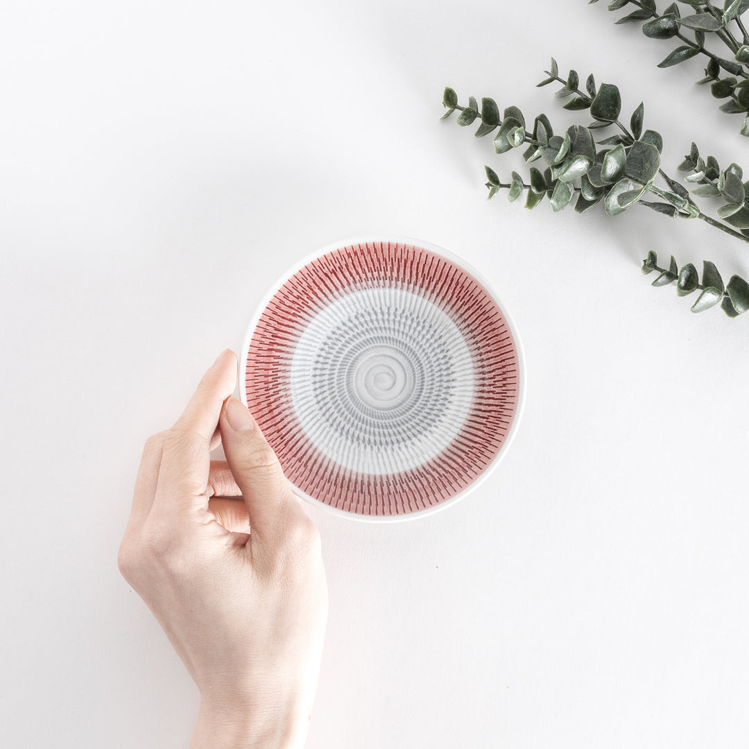 A hand holds the red dessert plate, displaying its striking spiral-striped design from above.