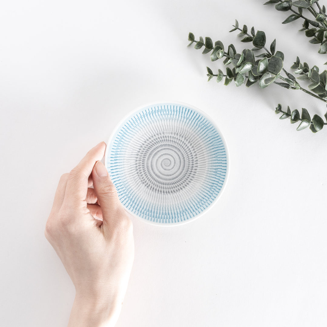 A hand holds the light blue dessert plate, showing its intricate spiral-striped pattern from a top-down angle.