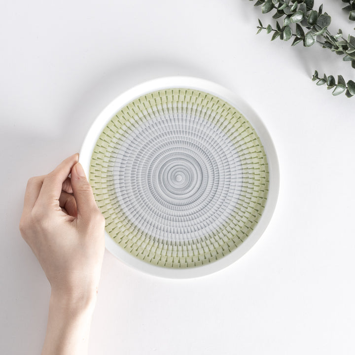 A hand holding the plate from above, showing the light green spiral design and smooth edges.