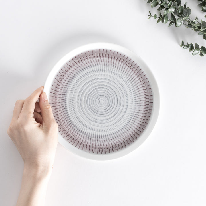 A hand holding the plate from above, showing the light purple spiral design and smooth edges.