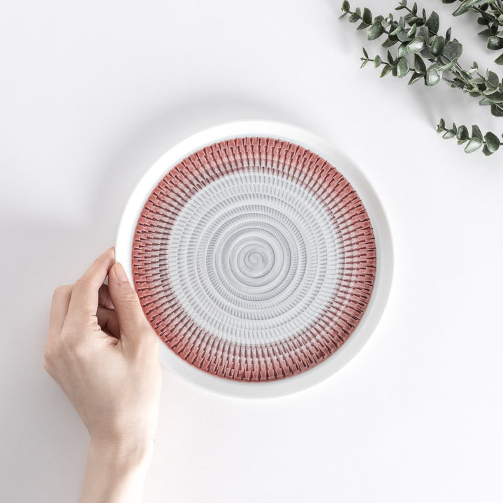 A hand holding the plate from above, showing the red spiral design and smooth edges.