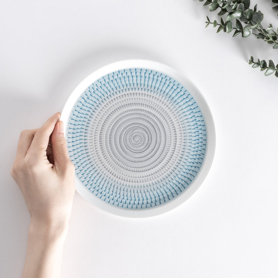 A hand holding the plate from above, showing the light blue spiral design and smooth edges.