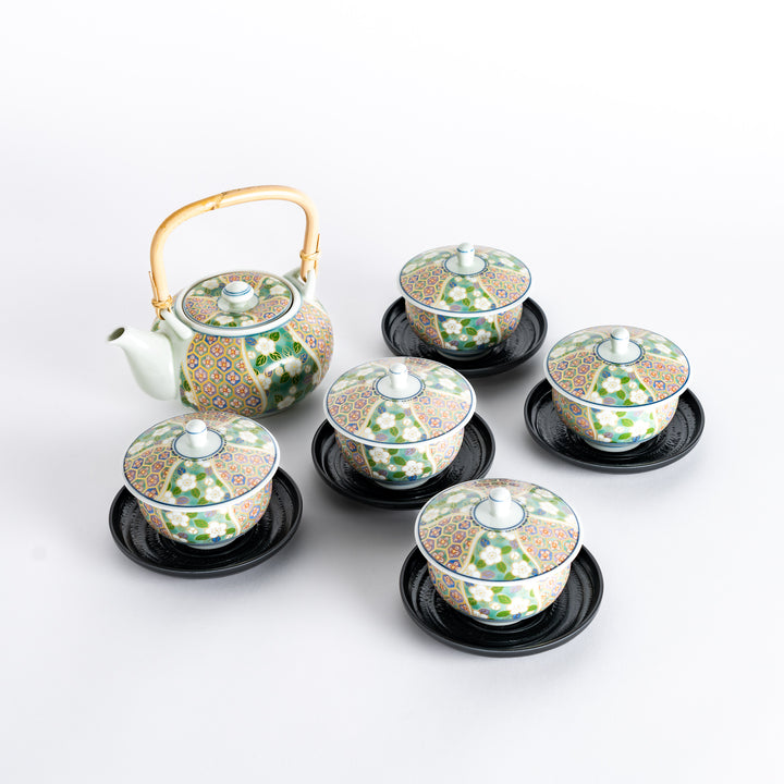 A complete tea set with bamboo-handled teapot and five floral pattern cups with lids, placed on black saucers. Green and pink design.