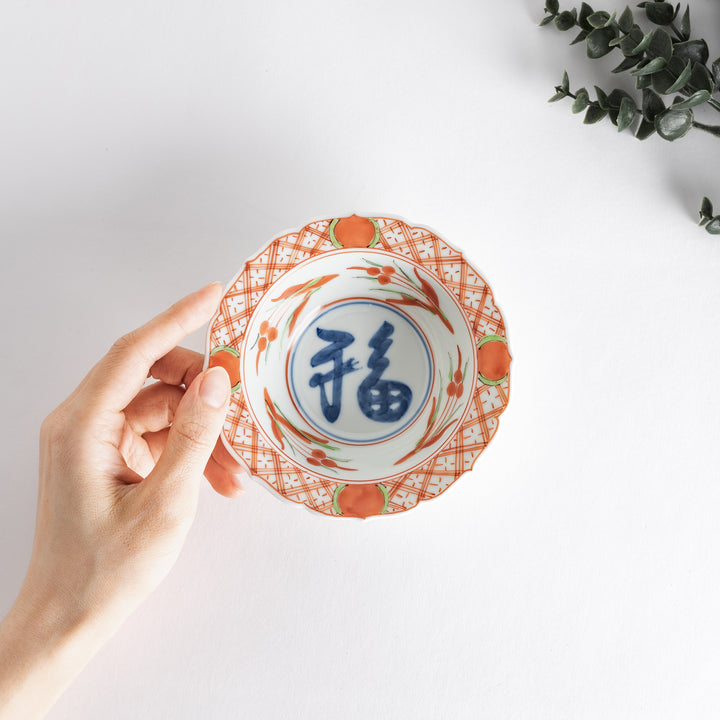 A dessert bowl with bold red and green designs around the rim, with a large blue kanji character in the center representing "fortune."