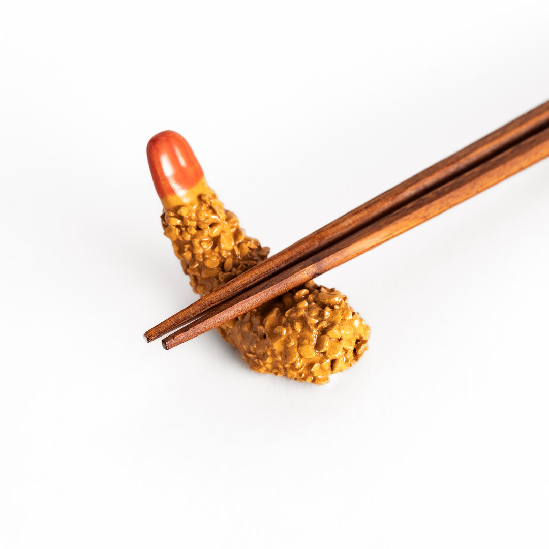 Close-up view of chopsticks placed on the fried shrimp chopsticks rest, emphasizing the intricate crispy coating and smooth red tip.