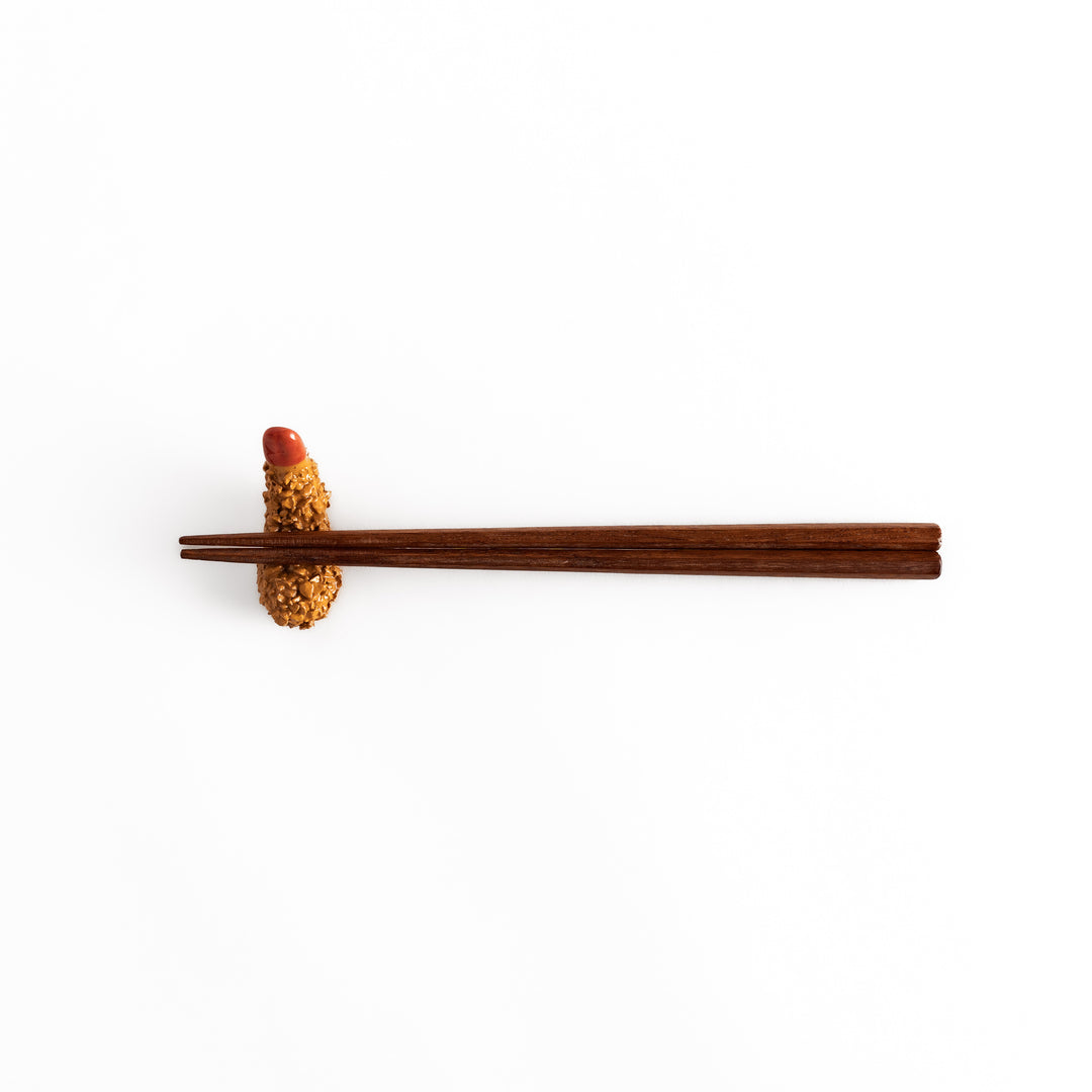 Distant view of chopsticks resting on the fried shrimp chopsticks rest, highlighting its realistic golden texture and red accent.