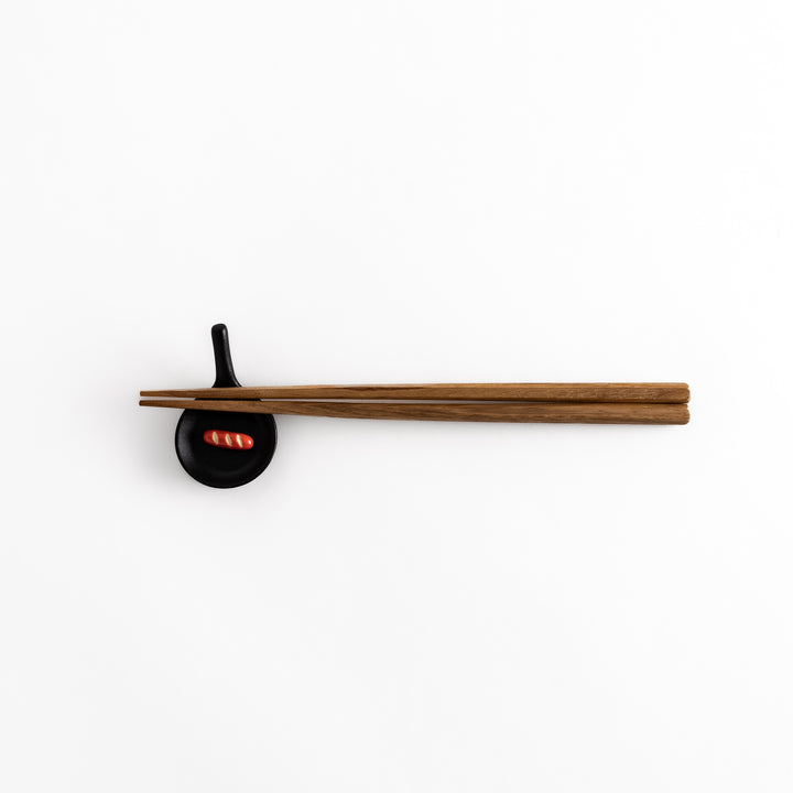 Pull-back view of a black frying pan-shaped chopstick rest with chopsticks resting on it, showcasing its practical use.