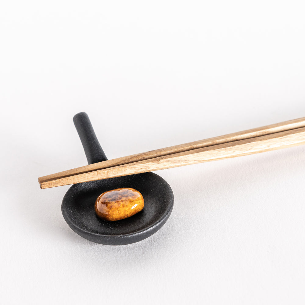 Close-up shot of a small black frying pan chopstick rest with a realistic hamburger patty, with chopsticks placed on top at an angle.