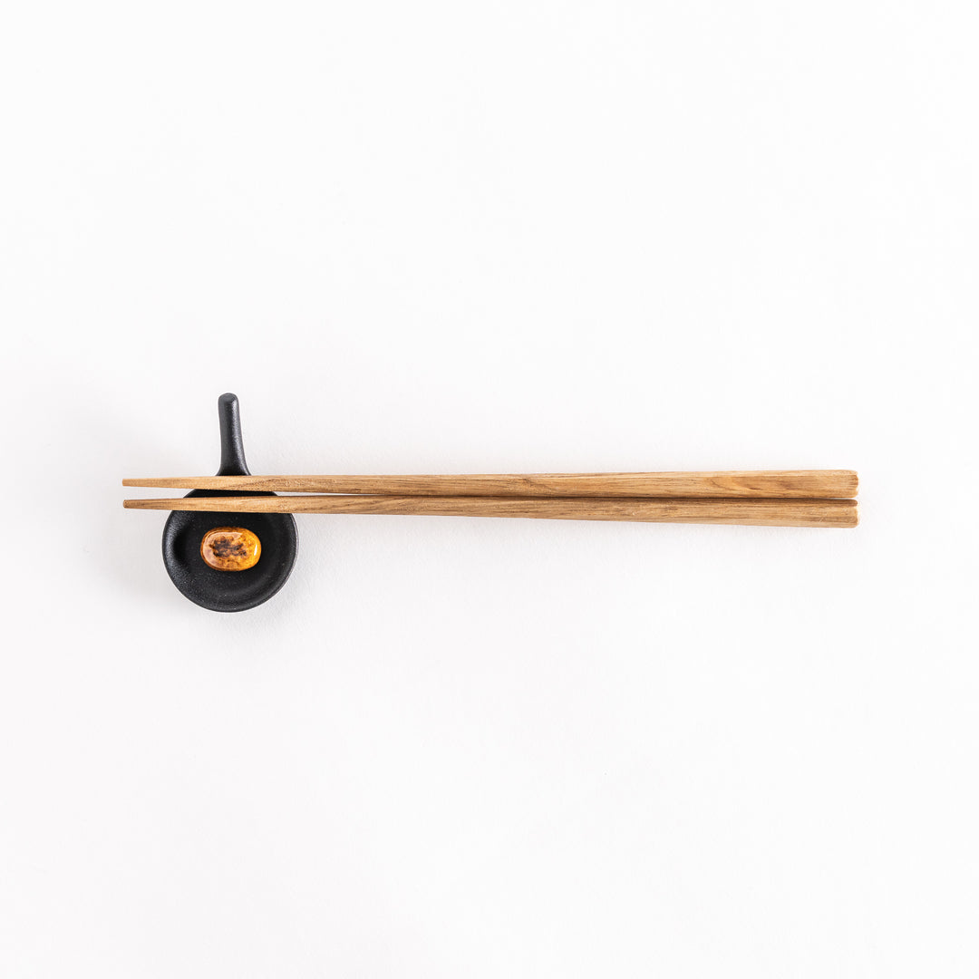 Wide shot of a small black frying pan chopstick rest with a hamburger patty inside and chopsticks placed gently across, captured from a slightly higher angle.