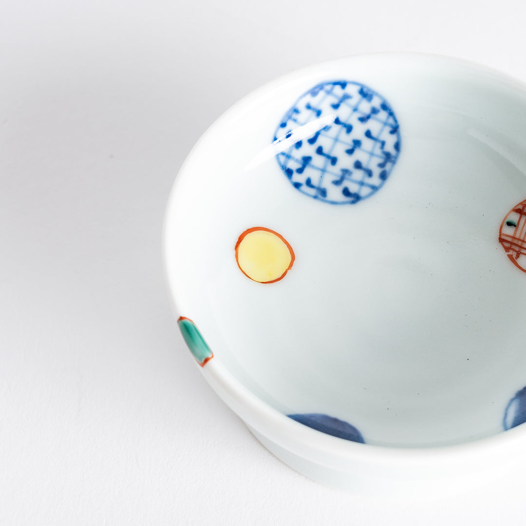 A small, round raised sauce dish featuring geometric circles in various colors, providing a textured, artistic design.