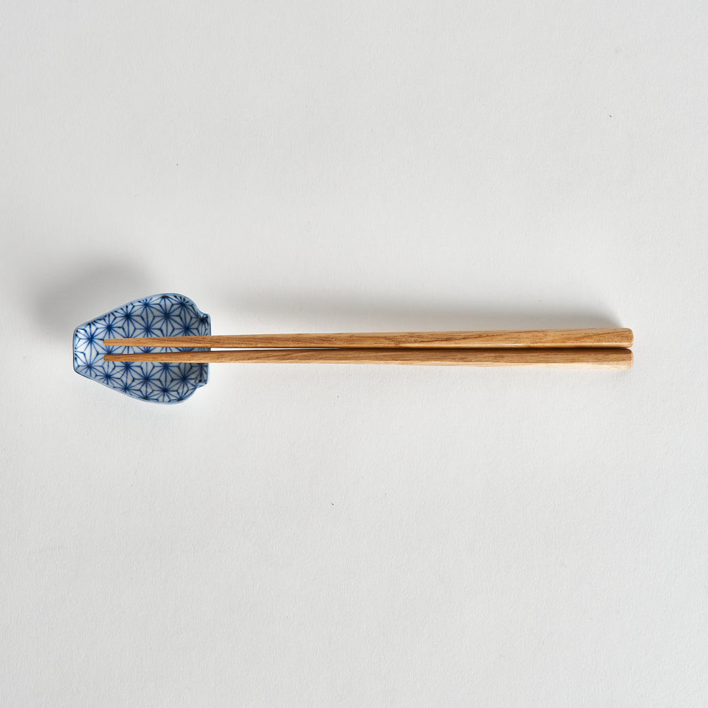 Chopsticks placed on a mini sauce dish with a blue and white geometric star pattern, the dish featuring curved edges and a small lip.