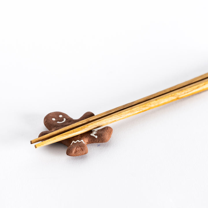 Close-up view of a gingerbread man-shaped chopstick rest with chopsticks resting, highlighting the smiling face and icing details on the figure.