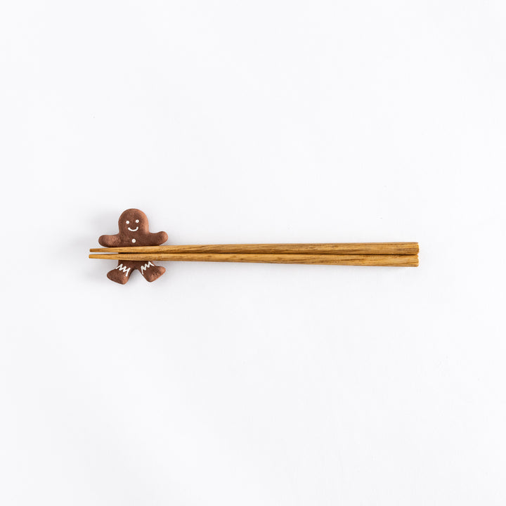 Top view of a gingerbread man-shaped chopstick rest with chopsticks resting on top, showing the details of the icing on the figure.