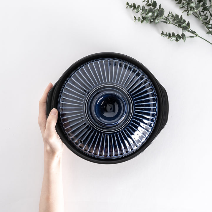 Top view of a blue donabe pot held by hand, highlighting the intricate ribbed lid design.