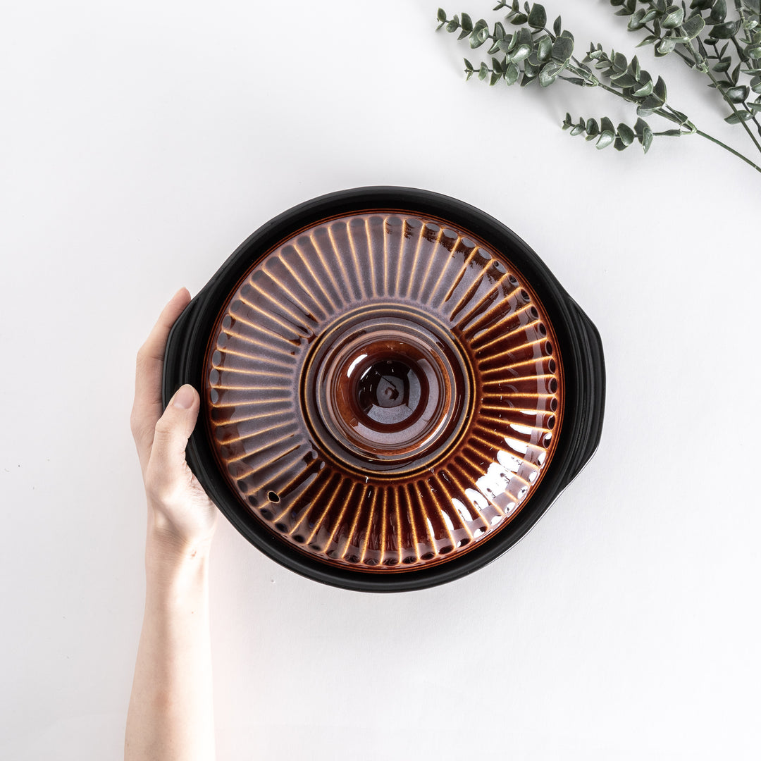 Top view of a brown donabe pot held by hand, showcasing the ribbed lid's natural glaze.