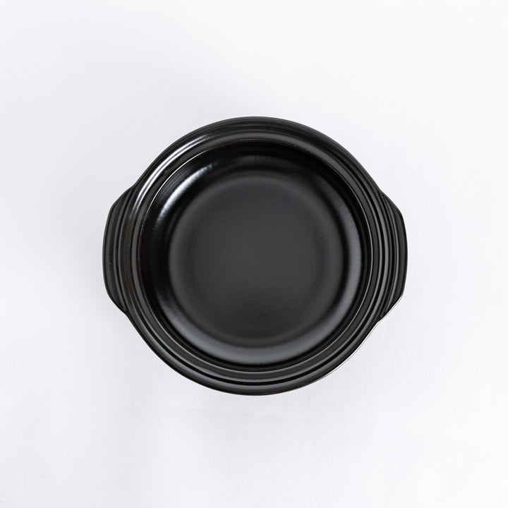 Top-down view of a white donabe pot with the lid removed, displaying the wide black interior.