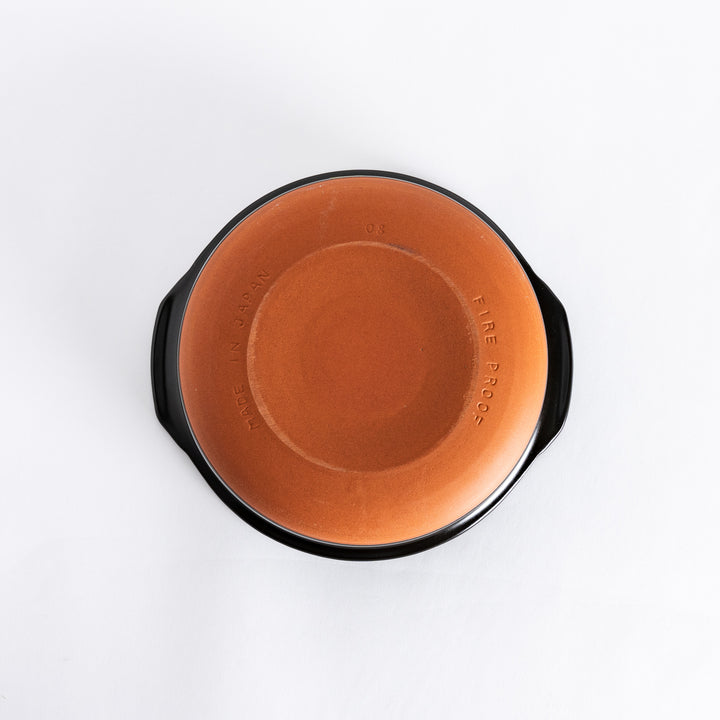 Underside of a brown donabe pot showing its unglazed ceramic base with a warm brown finish.