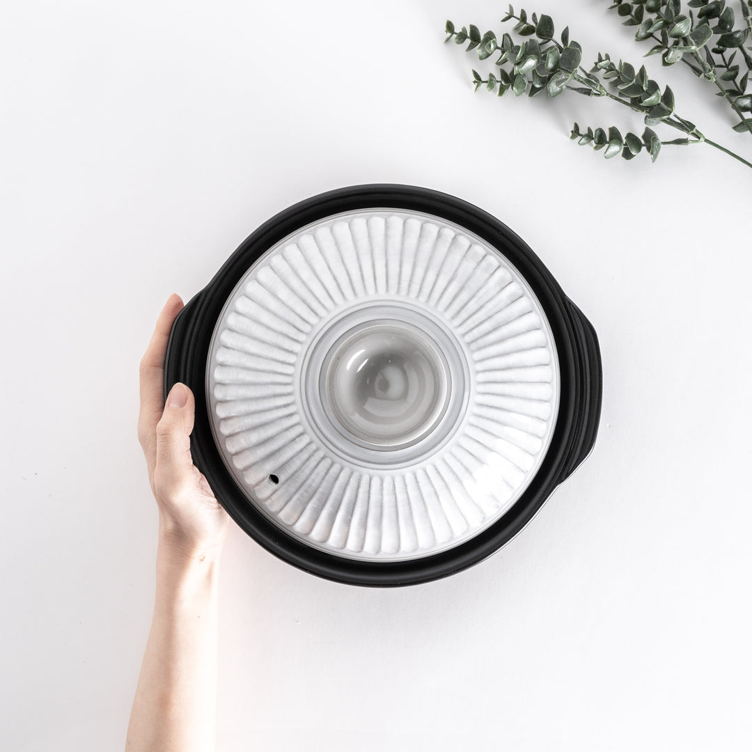 Top view of a white donabe pot held by hand, showcasing the ribbed lid design.