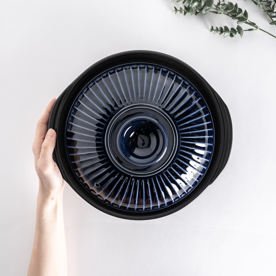 Top view of a blue donabe pot held by hand, highlighting the intricate ribbed lid design.