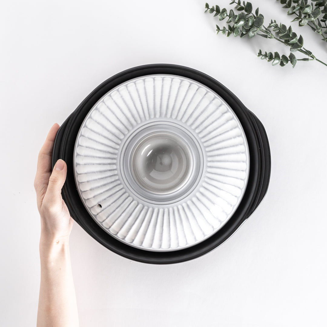 Top view of a white donabe pot held by hand, showcasing the ribbed lid design.