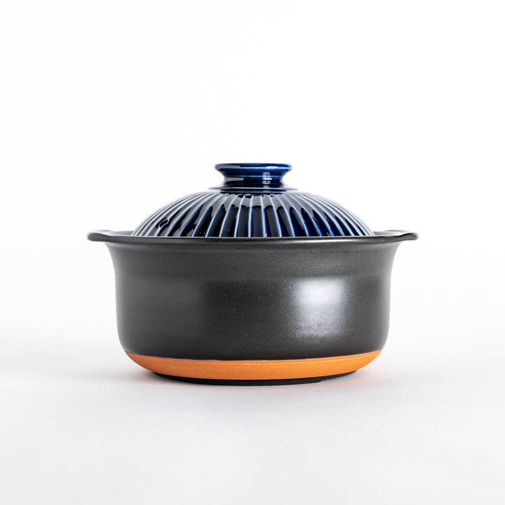 Side view of the donabe, displaying its rounded matte black body and ribbed navy blue lid.