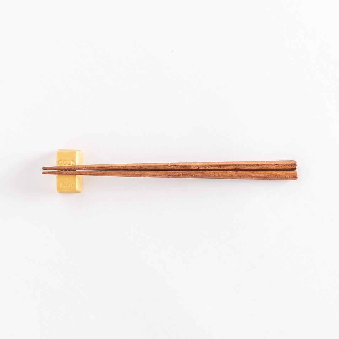 A wide view of the gold bar-shaped chopstick rest with chopsticks placed across it, emphasizing its realistic details.