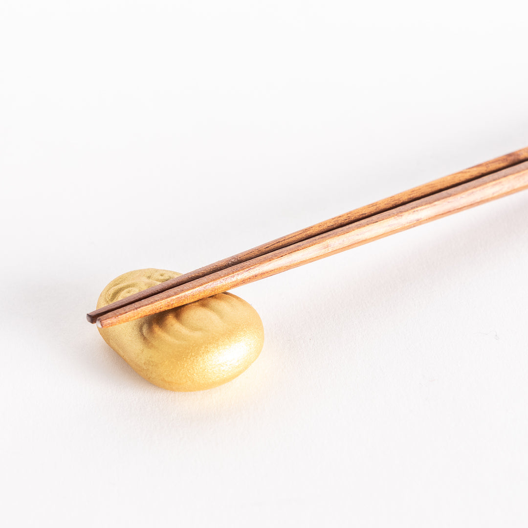 A close-up view of a gold Daruma doll-shaped ceramic chopstick rest with chopsticks resting across its surface.