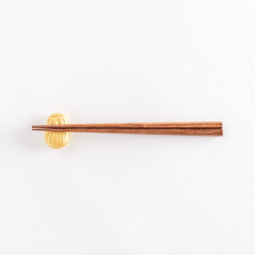 A wider view of the gold Daruma doll-shaped chopstick rest with chopsticks placed on it, highlighting its intricate details.