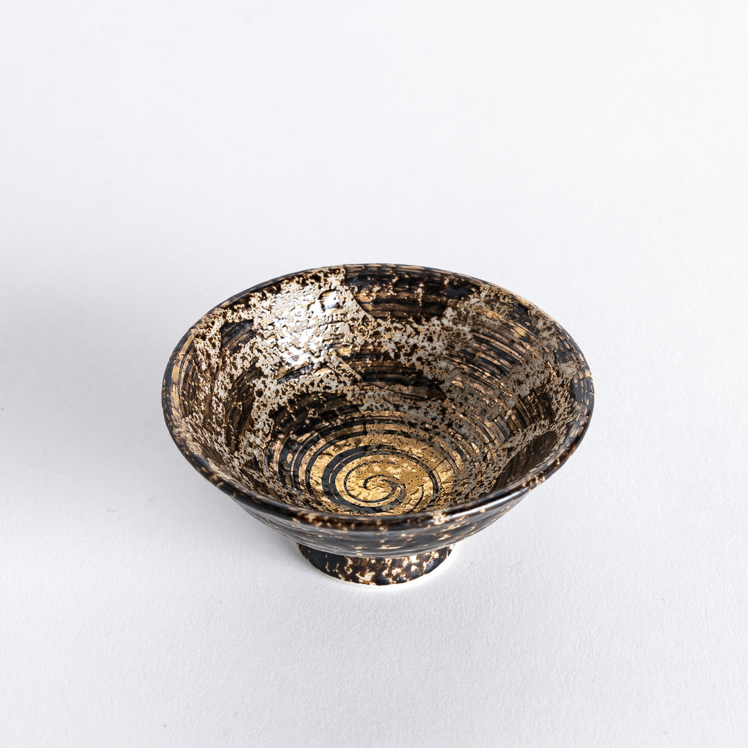 Slightly angled view of the sake cup showing its golden spiral design and rustic, textured surface.