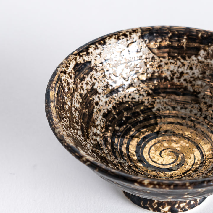 Close-up shot of the sake cup showing the detailed golden spiral pattern inside and the textured exterior.