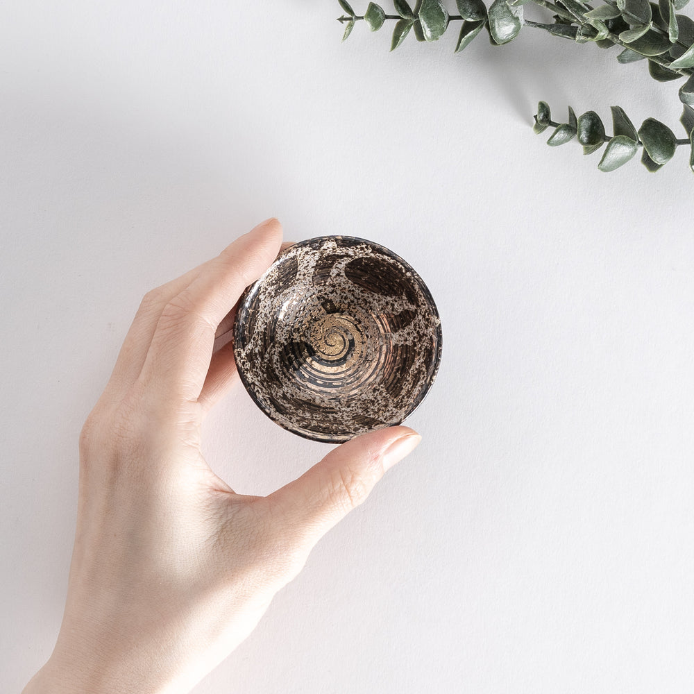 Top-down view of the sake cup held in hand, showing its rustic texture and golden spiral design.