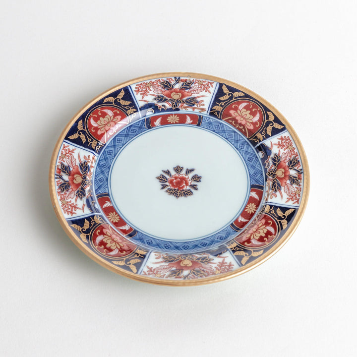 A small Imari-style porcelain plate featuring a central floral design and elaborate red, blue, and gold patterns around the rim.