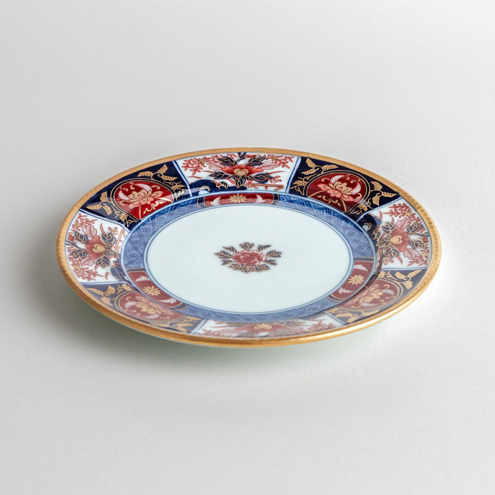 A small Imari-style porcelain plate featuring a central floral design and elaborate red, blue, and gold patterns around the rim.