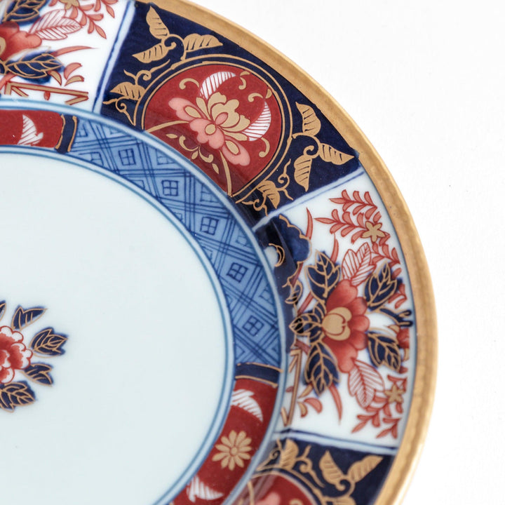 A small Imari-style porcelain plate featuring a central floral design and elaborate red, blue, and gold patterns around the rim.