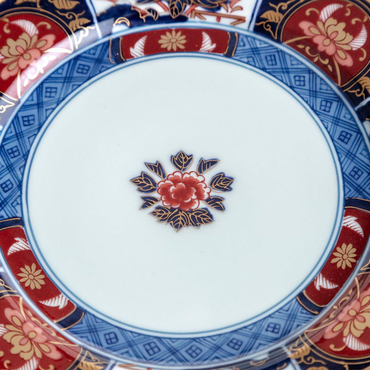 A small Imari-style porcelain plate featuring a central floral design and elaborate red, blue, and gold patterns around the rim.