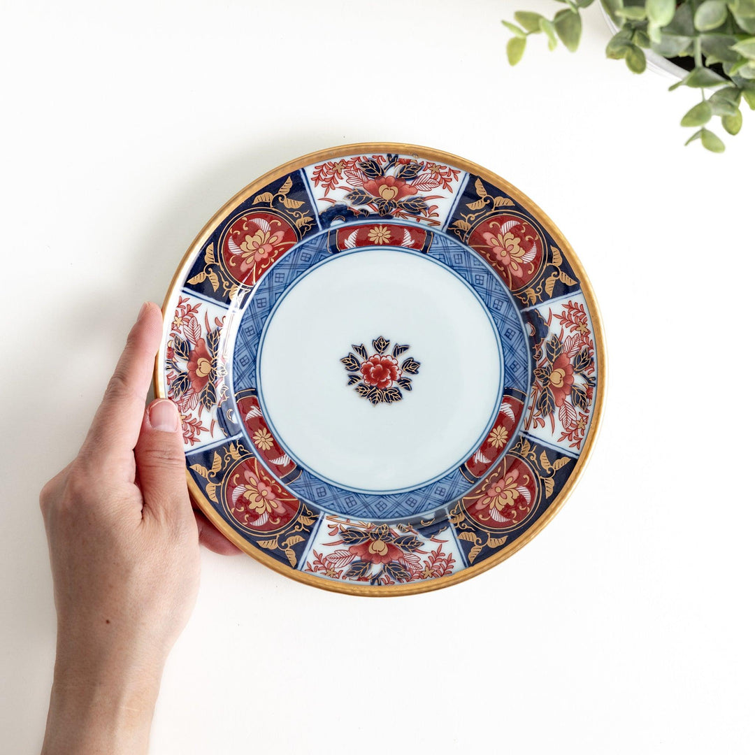 A small Imari-style porcelain plate featuring a central floral design and elaborate red, blue, and gold patterns around the rim.