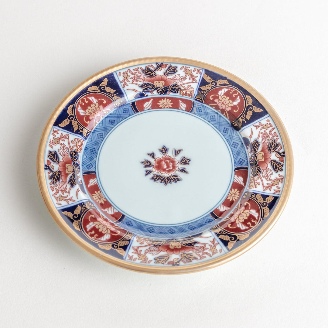 A smaller porcelain plate with a rich Imari-style design, showcasing a central floral motif and alternating sections of red and blue patterns with gold accents.