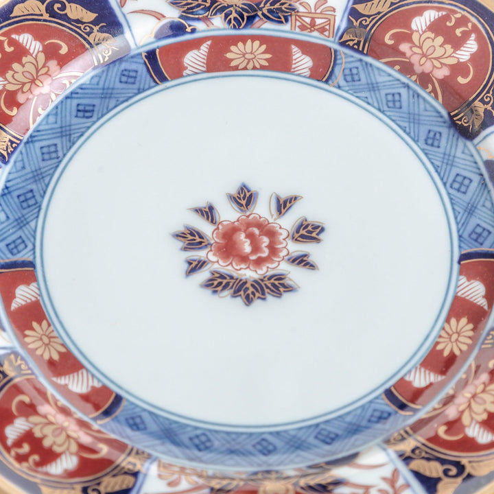 A smaller porcelain plate with a rich Imari-style design, showcasing a central floral motif and alternating sections of red and blue patterns with gold accents.