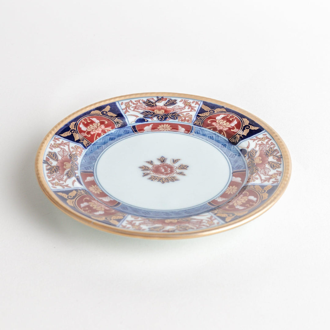 A smaller porcelain plate with a rich Imari-style design, showcasing a central floral motif and alternating sections of red and blue patterns with gold accents.