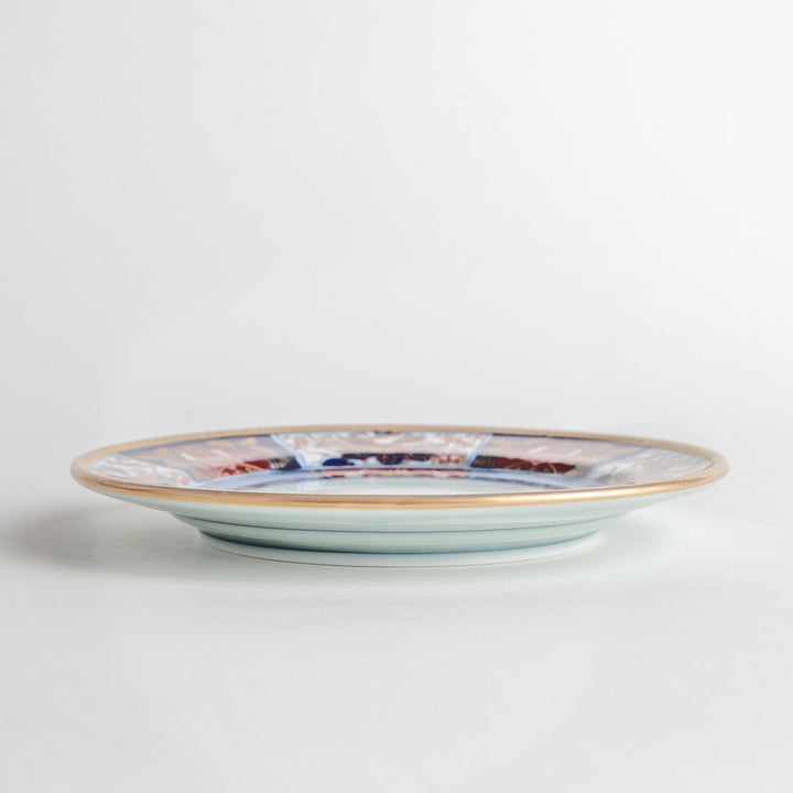 A smaller porcelain plate with a rich Imari-style design, showcasing a central floral motif and alternating sections of red and blue patterns with gold accents.