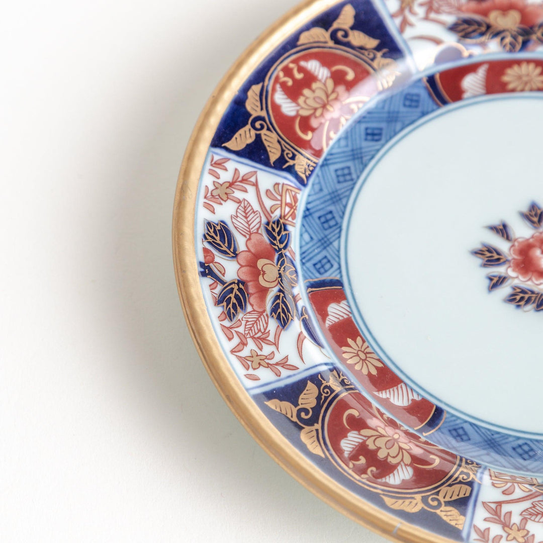 A smaller porcelain plate with a rich Imari-style design, showcasing a central floral motif and alternating sections of red and blue patterns with gold accents.