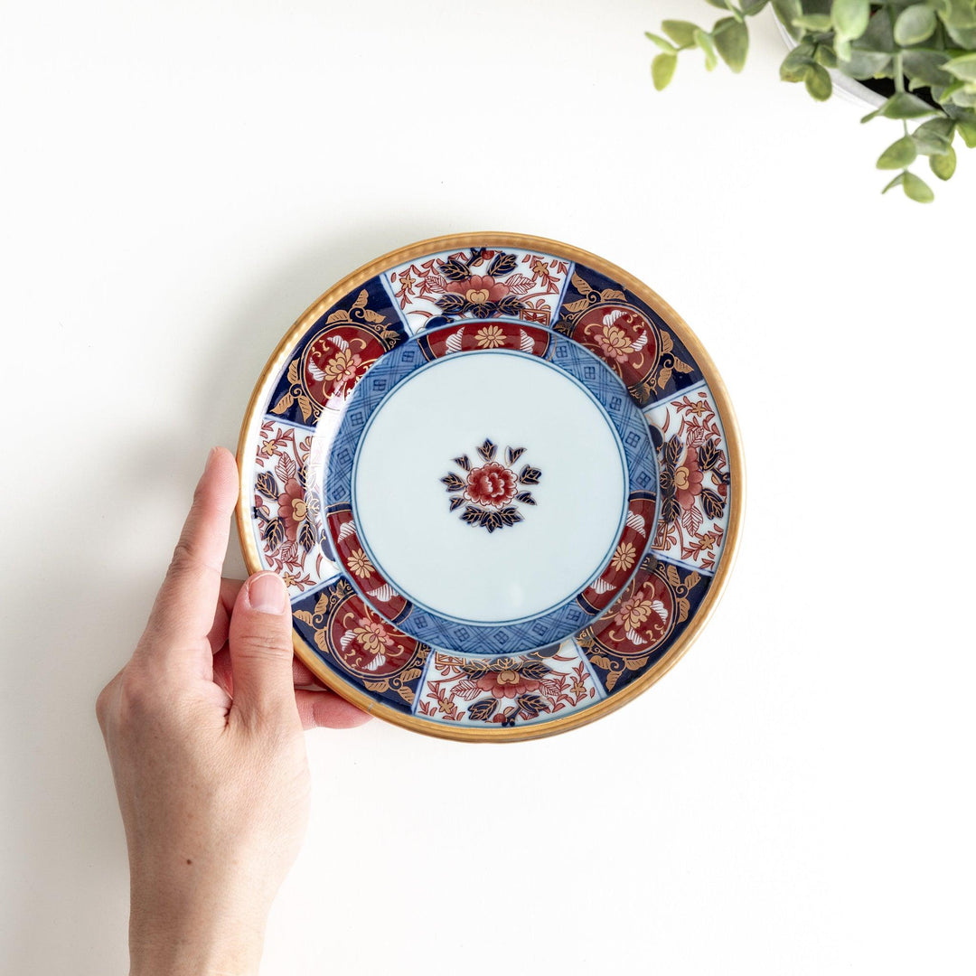 A smaller porcelain plate with a rich Imari-style design, showcasing a central floral motif and alternating sections of red and blue patterns with gold accents.