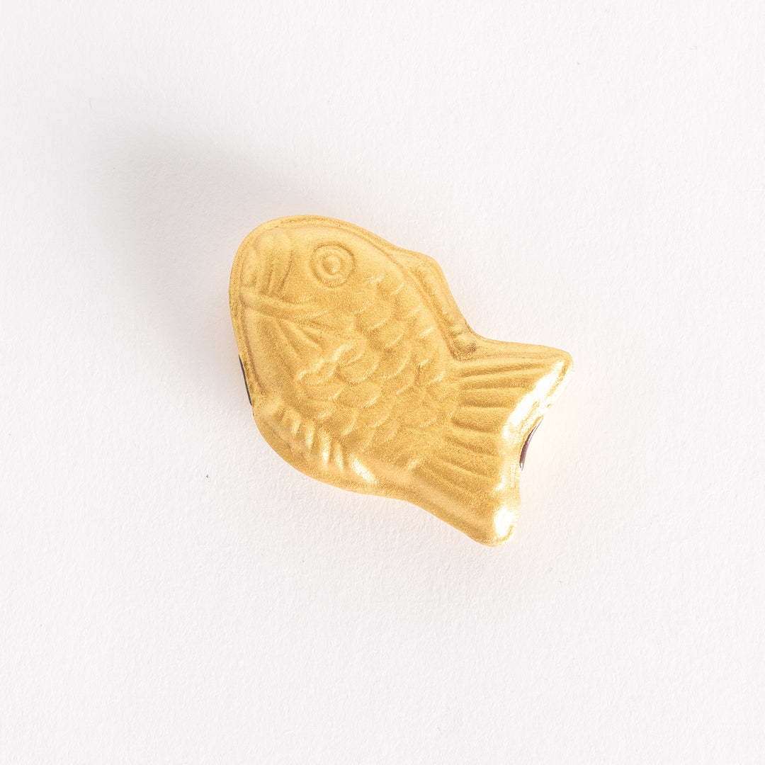 Top-down view of a golden taiyaki-shaped chopstick rest on a white background, showcasing its intricate fish design.