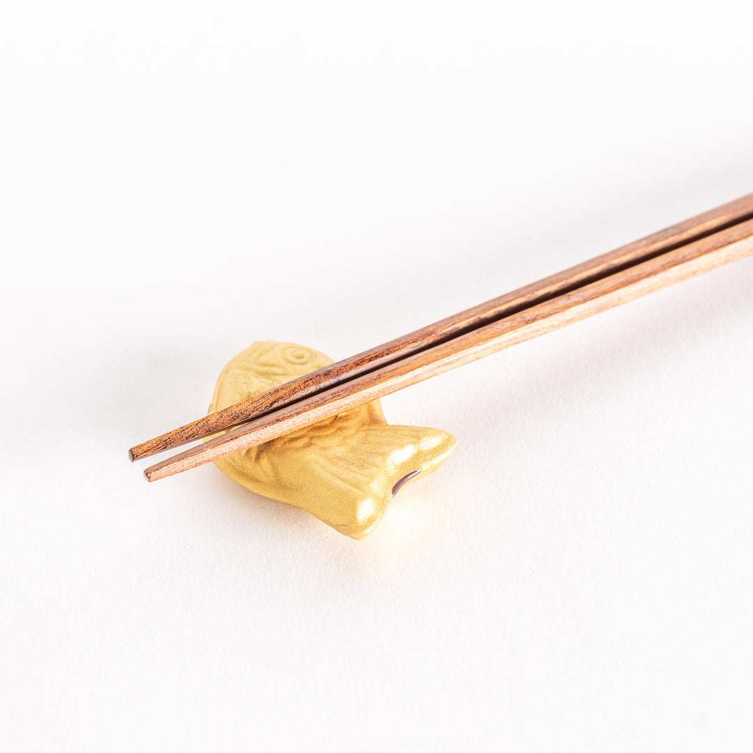 Close-up view of a golden taiyaki-shaped chopstick rest with a pair of chopsticks resting on it.